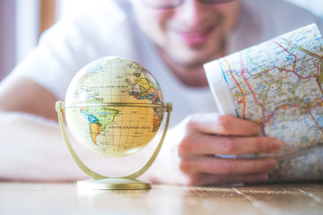 Junger Mann plant Weltreise, Globus und Landkarte
