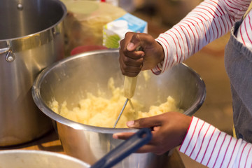 Hand mashhing potao in a large metal bowl
