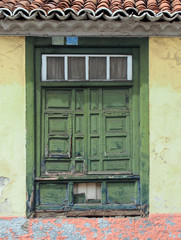Fototapeta na wymiar old traditional green painted window with closed shutters with peeling distress and damage on a light yellow wall in spain