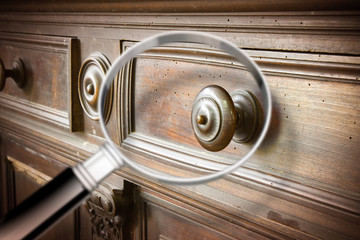Detail of an antique wooden italian furniture just restored with a magnifying glass on foreground looking for woodworm threat detection