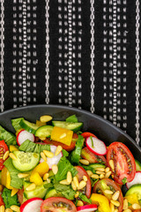 Salad of fresh vegetables with pine nuts on a black plate.