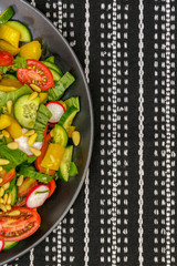 Salad of fresh vegetables with pine nuts on a black plate.