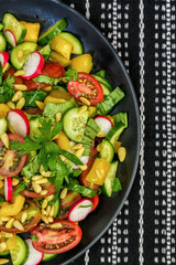 Salad of fresh vegetables with pine nuts on a black plate.