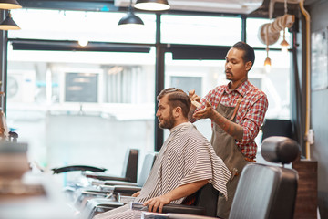 Concentrated thai barber going to make a haircut for a bearded man