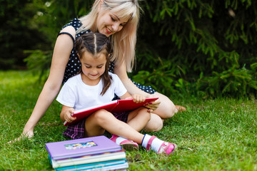 Pretty young mother reading book to her little daughter at green meadow