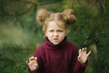 A sweet and funny girl in a sweater builds frightening faces in an autumn park