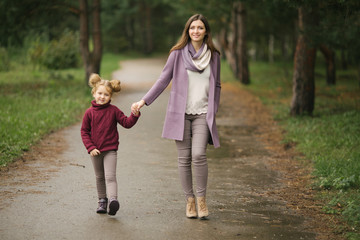 Fototapeta premium A young mother and her little daughter are walking along the path in the park