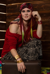 Cheerful hippie boho redhead woman poses with old suitcase on a wooden wall background