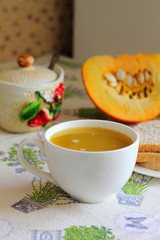 Pumpkin soup in white mug on table.