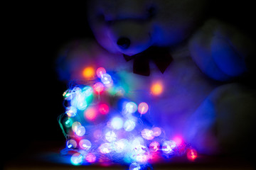 Fototapeta na wymiar White teddy bear with Blurred and defocused christmas colorful lights, abstract magic background