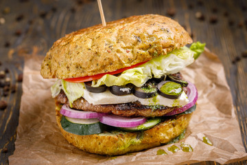An unusual burger with a kettle and a salad of vegetables on kraft paper and a dark wooden background.