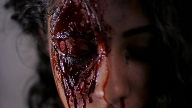 Scary portrait of young girl with Halloween blood makeup. Beautiful latin woman with curly hair looking into camera. Slow motion.