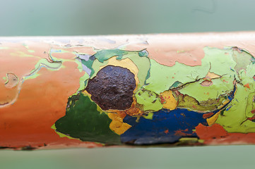 Peeling paint on a metal bar. Multiple layers of colored paint.