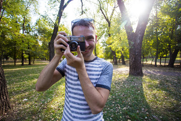 Young man taking pictures on retro camera in city park