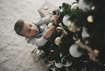 Boy decorating a christmas tree - obrazy, fototapety, plakaty