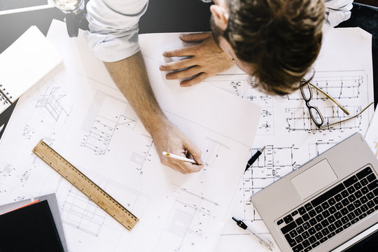 Man working on construction plan at desk, top view