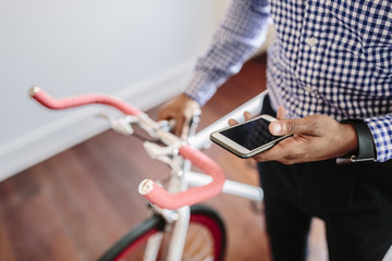 Close-up of man checking the phone while holding a bike indoors