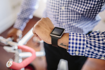 Close-up of man checking the smartwatch while holding a bike indoors