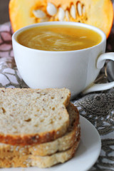Pumpkin soup in white mug on table.