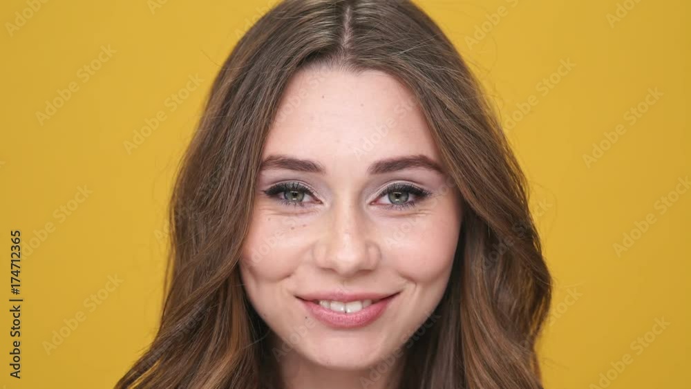 Poster close up view of smiling brunette woman looking at the camera over orange background