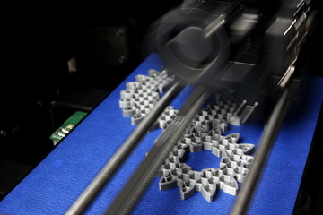 FDM 3D-printer manufacturing spur gears from silver-gray filament on blue print tape - diagonal top...