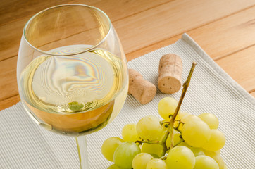 Glass of White Wine with a Bunch of White Grapes and two Corks on a Table. 