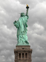 Statue of liberty seen from the back with a grey and cloudy sky as background in Manhattan, New York City.