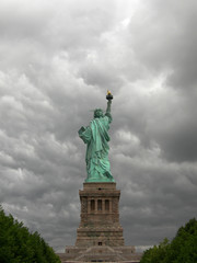 Statue of liberty seen from the back with a grey and cloudy sky as background in Manhattan, New York City.