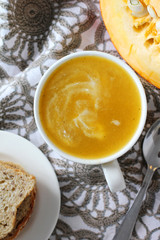 Pumpkin soup in white mug on table.