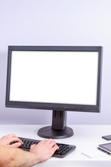 Fototapeta premium White blank pc monitor on white desk, and male hands writing on black keyboard.