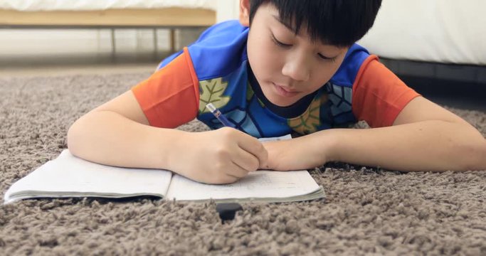 Cute asian boy rest on floor and doing homework at home with smile face.
