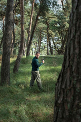 Man with pistol standing in pine forest. Side view.