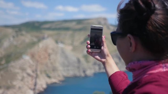 Young beautiful girl is taking pictures on the phone of a beautiful landscape of mountains and the sea. HD, 1920x1080, slow motion.