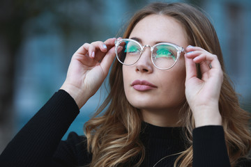 Myopia, close-up portrait of young woman student in eyeglasses for good vision looking up, blue building background - 174722569