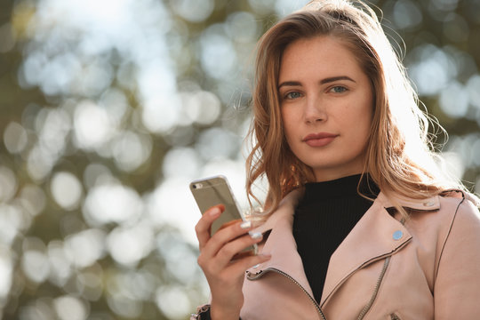 Young woman portrait with smart phone against blurred tree background