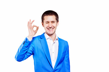 Closeup isolated portrait of young man in blue suit showing OK gesture at white background.