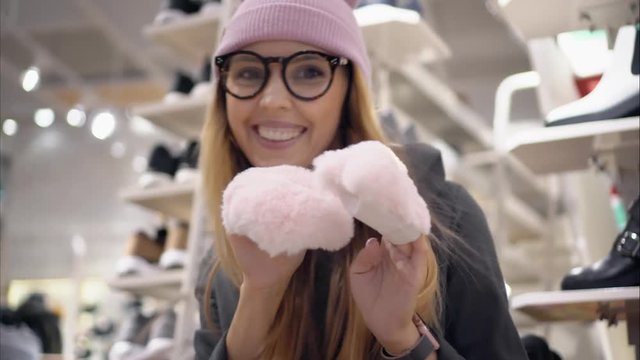 A stylish hipster girl in fashionable glasses and a hat dances in a shoe store