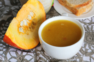 Pumpkin soup in white mug on table.