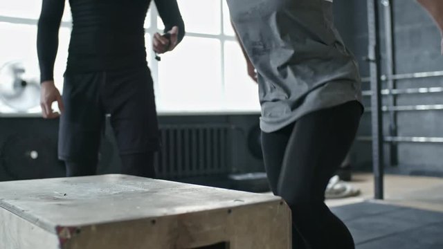 Closeup of woman jumping on box in gym during cross training with personal coach