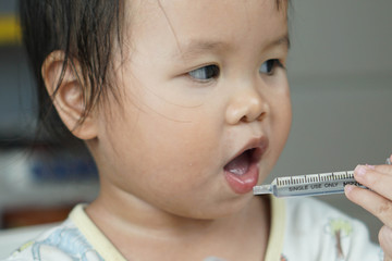Baby asian toddler girl feeding medicine by themself
