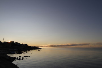 Beautiful sunrise over an arctic lake with fog on the horizon and sun peaking over buildings