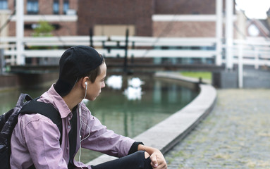 young man listening to music sitting on the sidewalk