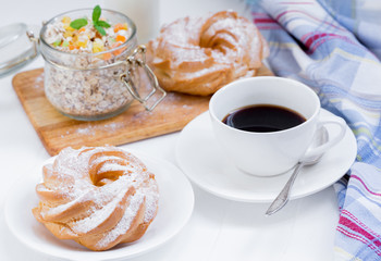 A cup of coffee, a granola, buns on a white background near a striped napkin