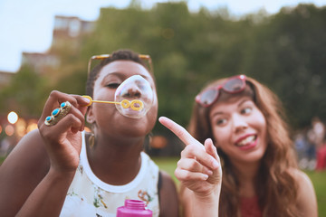 group of two diverse friends blowing soap bubbles at a summer music festival.
