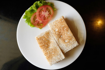 Top view of healthy sandwich toast with lettuce, fried pork, cheese and tomato on a black marble background.