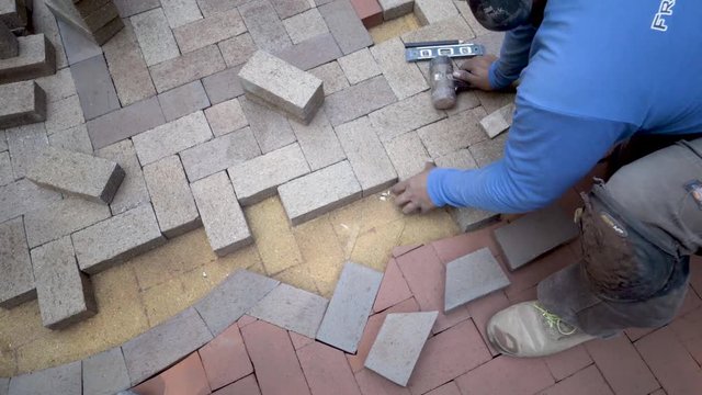 Putting brick pavers in place for the herringbone design in the two tone emblem, the artisan uses a rubber mallet to get them into their proper places.