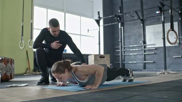 Zoom in of muscular woman doing push-ups in cross training gym under control of personal coach