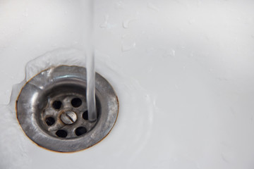 Save water! A jet of water gets directly into the drain hole in a white sink or bathtub.