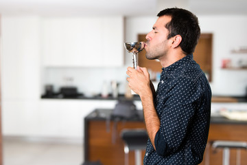 Brunette man holding a trophy inside house