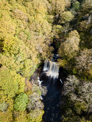Aerial view of a large watefall in a tree lined valley during the fall